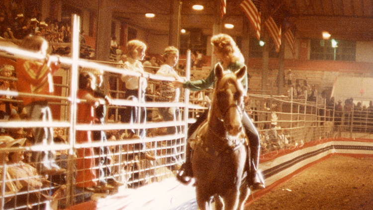 Reba on horseback talking to two young boys on fence 